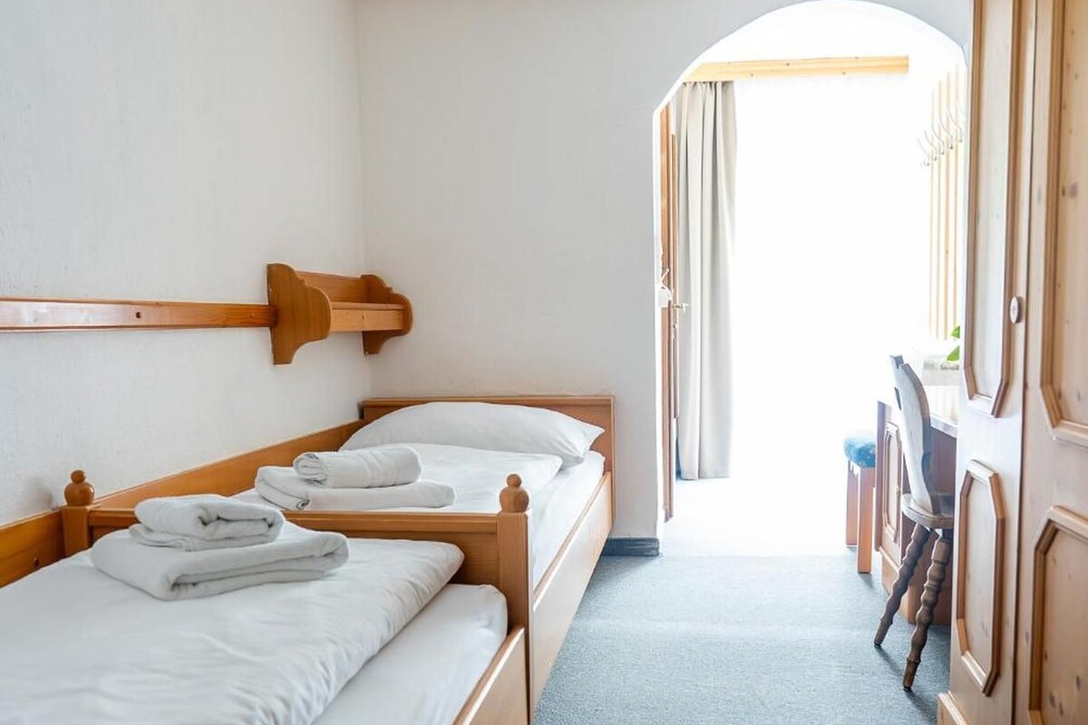 A hotel room with two wooden beds, a small wooden nightstand, a wardrobe, and a view through an arched doorway.