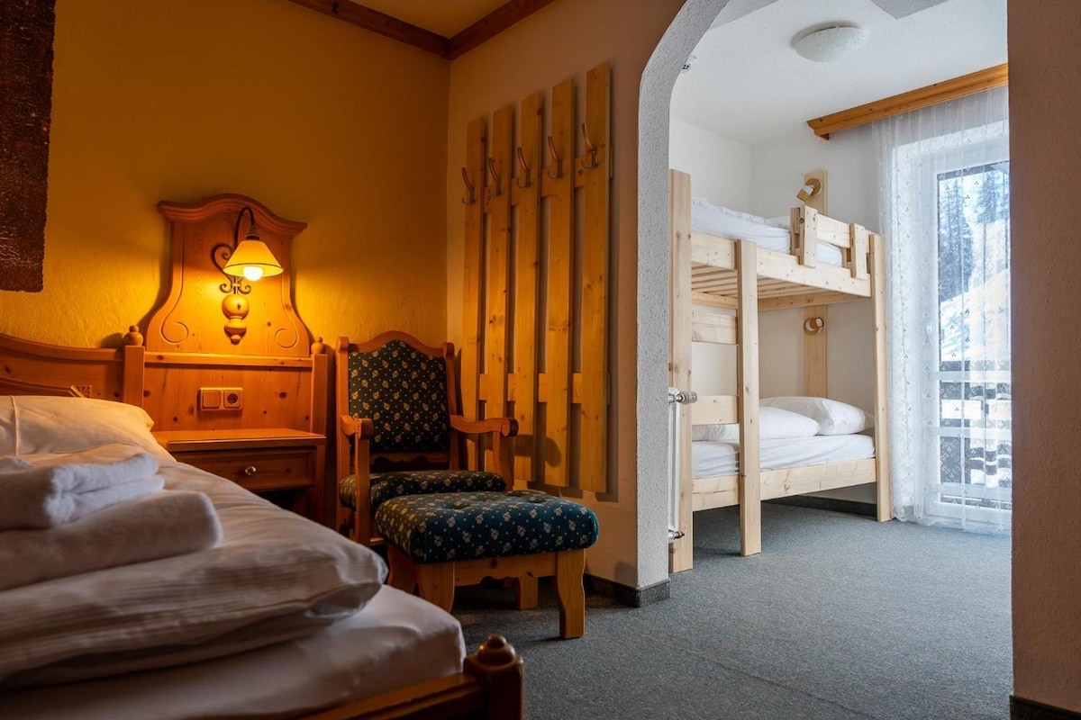 A hotel room with a bed, a chair, a wooden headboard, a wall-mounted lamp, and a bunk bed.