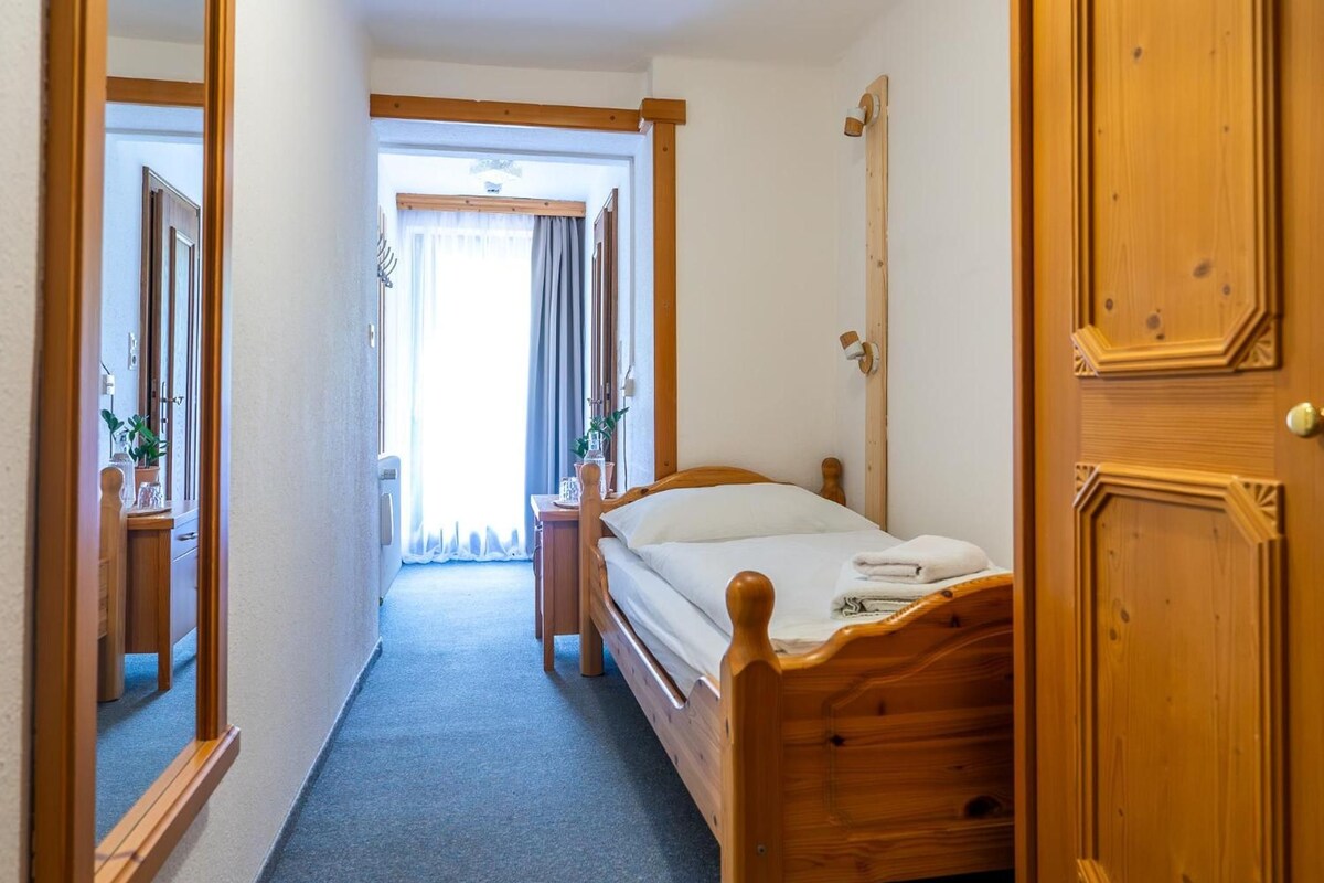 A hotel room with a wooden bed, a bedside table, a mirror, and a door.