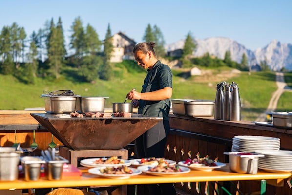 A chef cooking outdoors with a view of mountains in the background.