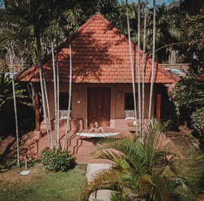 Ein Haus mit rotem Ziegeldach, umgeben von Palmen und einer kleinen Terrasse mit Tisch und Stühlen.