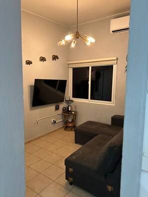 Ein Wohnzimmer mit einem an der Wand montierten Flachbildfernseher, einem Fenster mit Blick, einer Couch und einer Deckenleuchte.