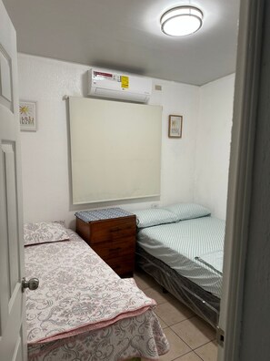Eine kleine, einfache Unterkunft mit einem Bett, einem Schminktisch und einem Fenster.