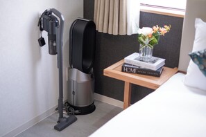 Ein Staubsauger, ein kleiner Tisch mit Buch und Vase sowie ein Bett in einem Hotelzimmer.