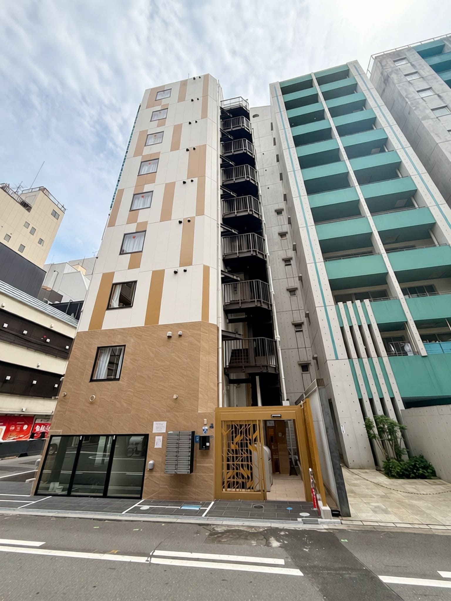 Un edificio de varios pisos con un diseño arquitectónico moderno, que presenta una combinación de paneles beige y blancos, una escalera destacada y una serie de balcones.