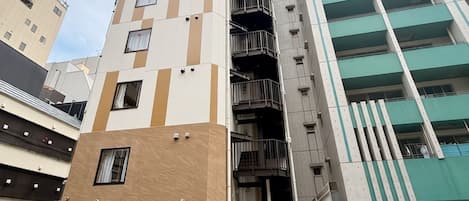 Edifício de vários andares com design arquitetônico moderno, combinando painéis bege e brancos, uma escadaria imponente e uma série de varandas.