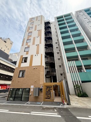 Ein mehrstöckiges Gebäude mit moderner Architektur, das eine Kombination aus beige- und weißen Fassadenelementen, eine markante Treppe und mehrere Balkone aufweist.