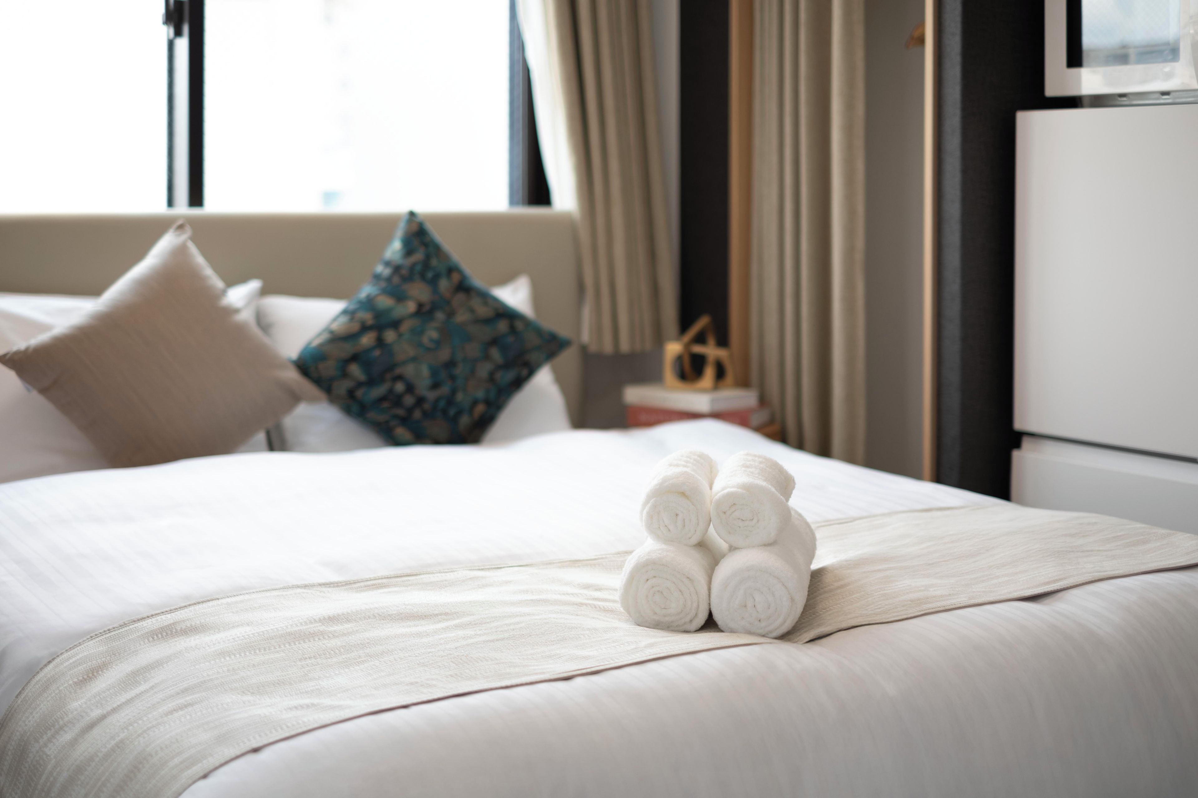 A neatly made bed with rolled towels, a pillow, and a decorative item on a bedside table.