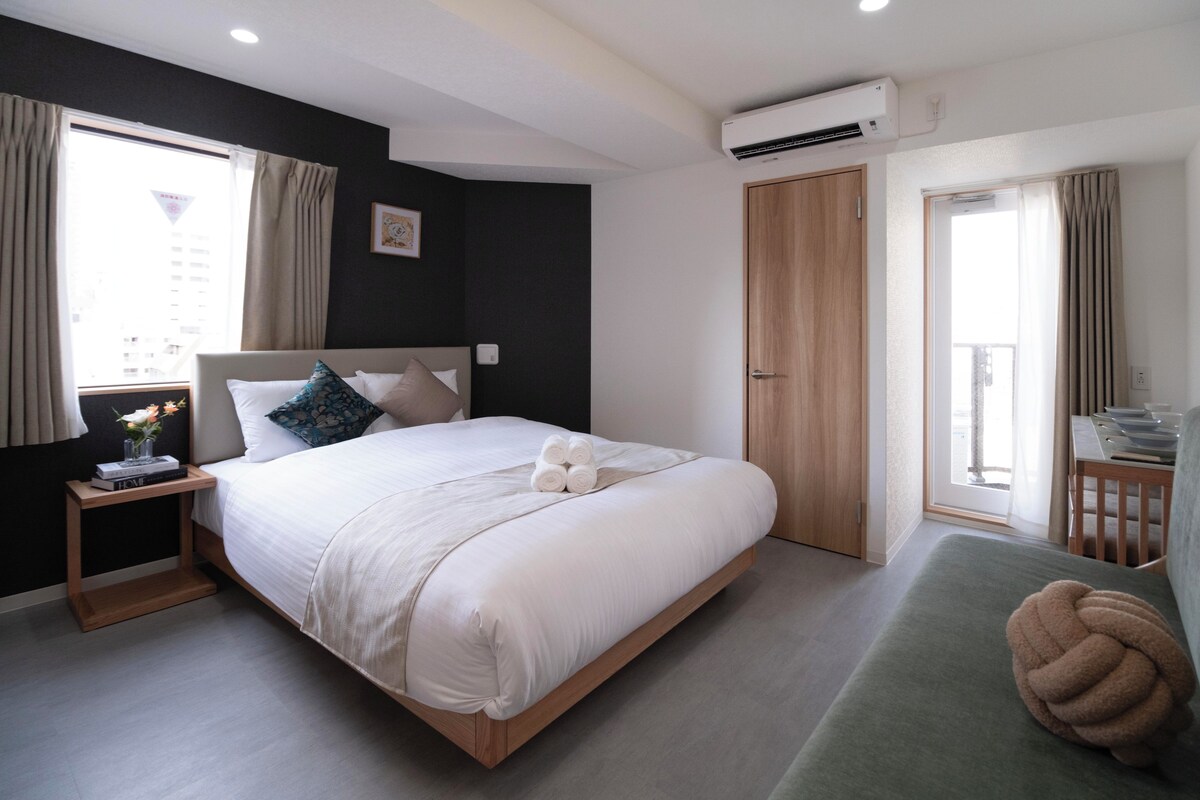 Ein modernes Hotelzimmer mit einem großen Bett, Nachttischen, einem grünen Sofa und Blick auf die Stadt.