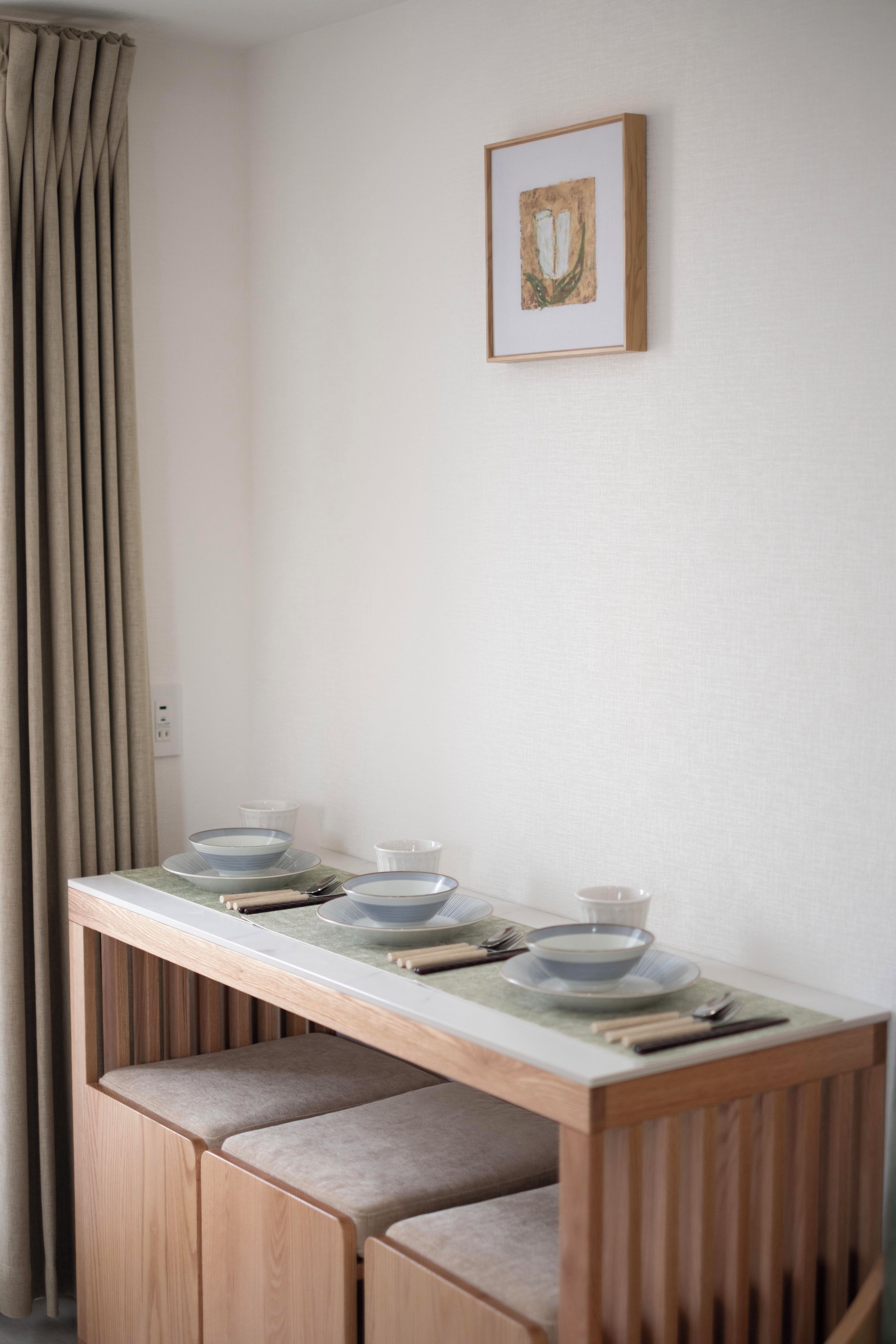 A dining area with a wooden table set for four, a bench, and a framed picture on the wall.
