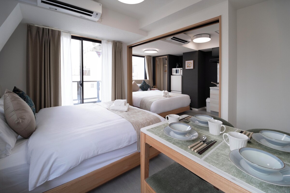 Ein Hotelzimmer mit einem großen Bett, einem kleineren Bett, einem Esstisch mit Tellern und Besteck sowie einer Klimaanlage.