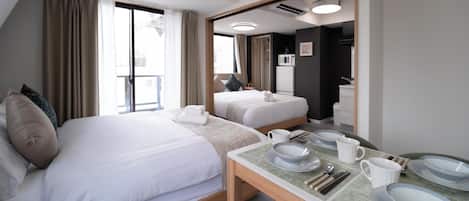 A hotel room with a large bed, a smaller bed, a dining table with plates and utensils, and an air conditioning unit.