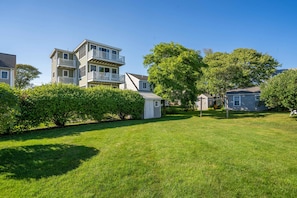 A residential area with a two-story house featuring a balcony, a well-maintained lawn, and mature trees. - Moody Surfer - Coastal Retreat (Wells)