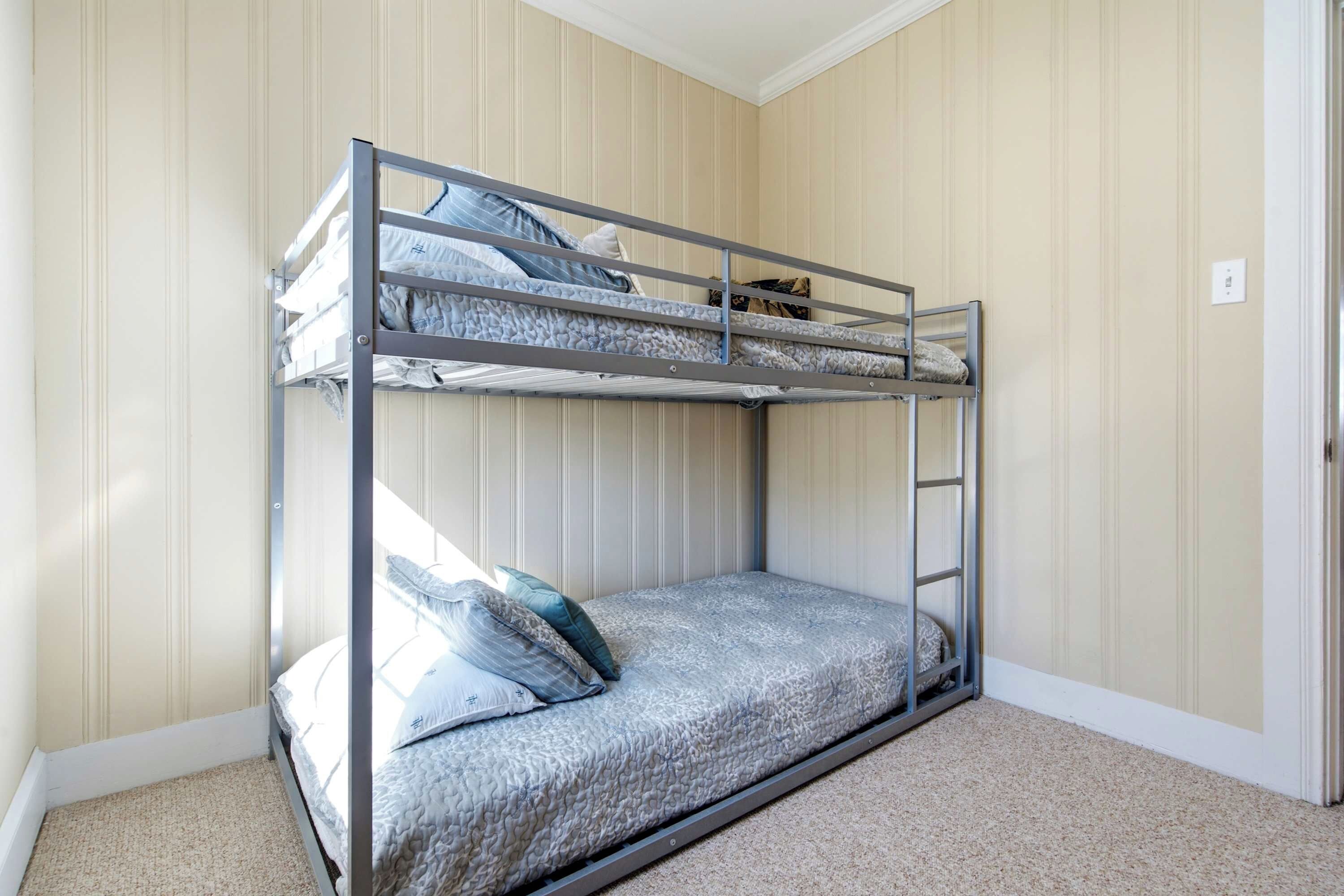 A bunk bed with a ladder, a single bed below, and a carpeted floor.