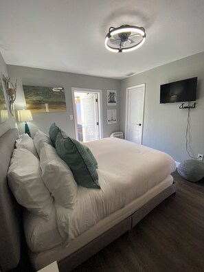 Une chambre à coucher avec un lit, un téléviseur, un ventilateur de plafond et des œuvres d’art accrochées aux murs.