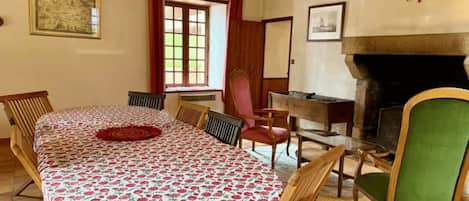 A room with a round table, chairs, a fireplace, and a window with curtains.