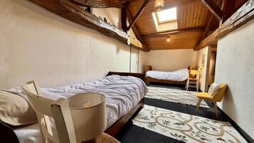 A cozy room with two beds, a chair, a lamp, and a patterned rug.