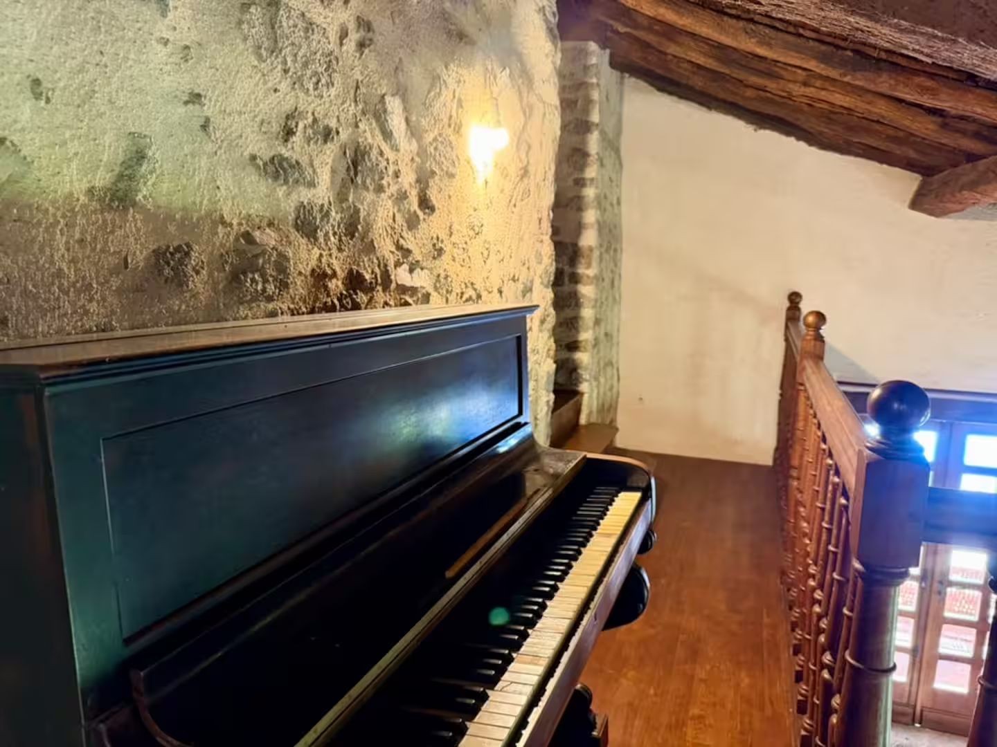 Un piano dans une pièce aux murs de pierre et à l’escalier en bois.