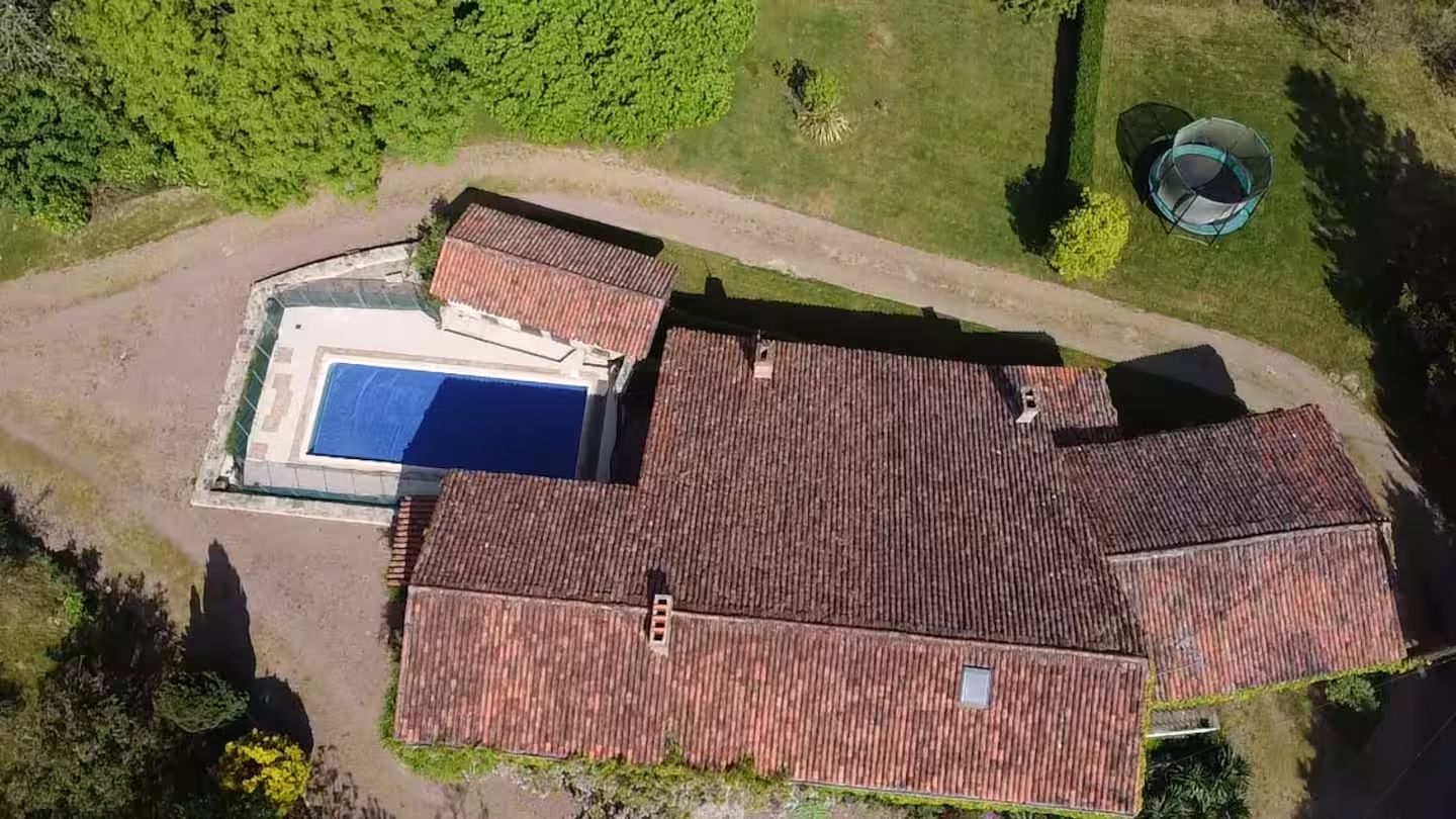 Vista aérea de uma propriedade com piscina, um amplo terraço coberto e telhado com telhas vermelhas.