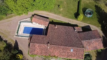 Vista aérea de uma propriedade com piscina, um amplo terraço coberto e telhado com telhas vermelhas.