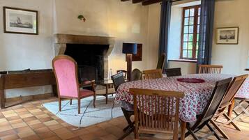 Un comedor con chimenea, sillas de madera, una mesa con mantel floral y un banco.