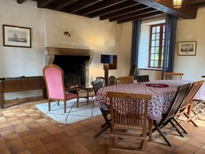 A dining room with a fireplace, wooden chairs, a table with a floral tablecloth, and a bench.