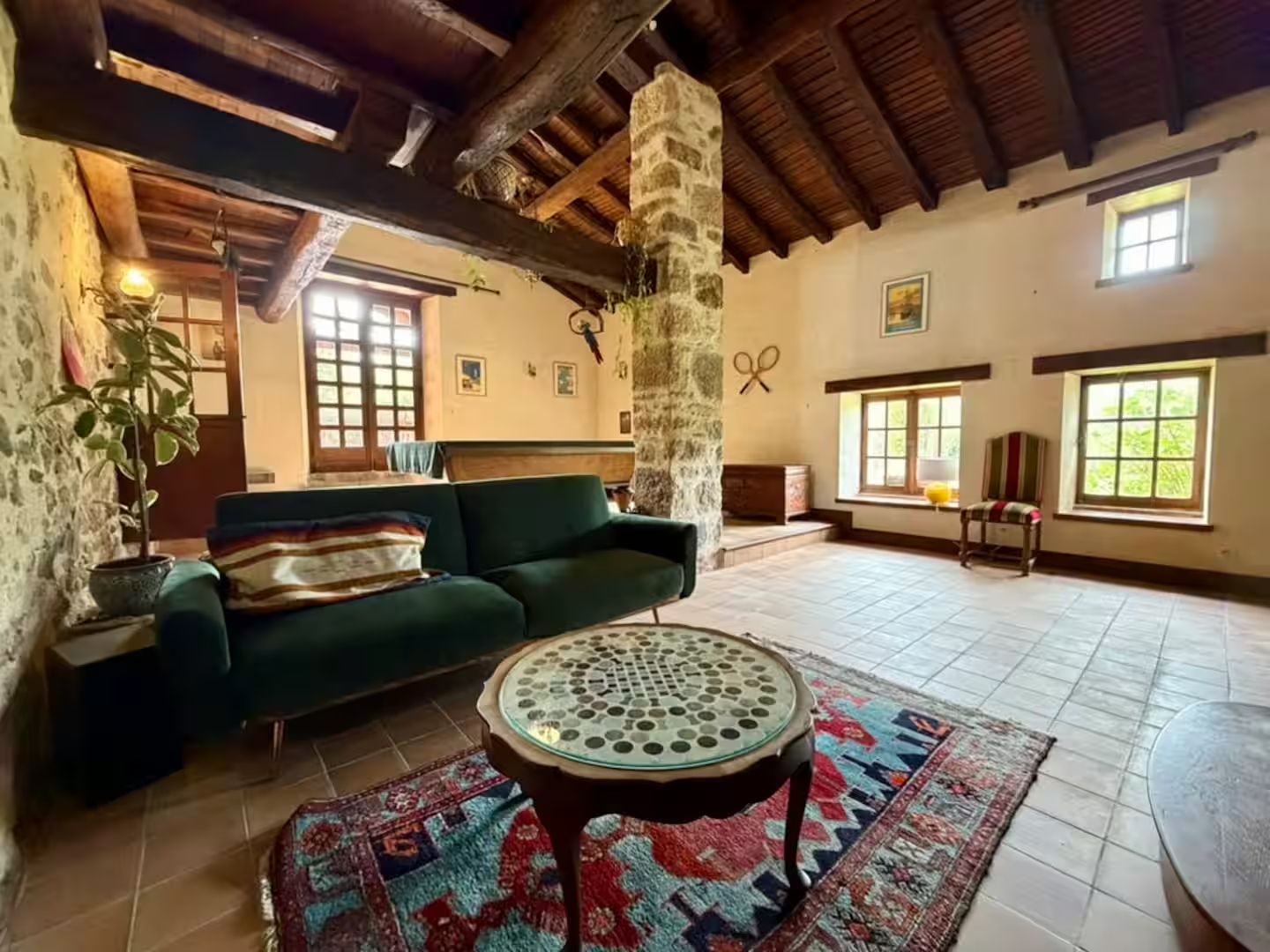 Um quarto espaçoso com um sofá verde, uma mesa redonda e um pilar de pedra.