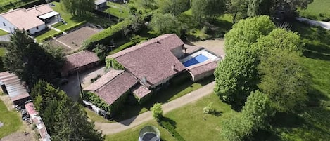 An aerial view of a residential property with a swimming pool, a covered outdoor seating area, and a well-maintained lawn.