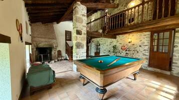 A pool table in a room with stone walls, a wooden ceiling, and a staircase leading to an upper level.