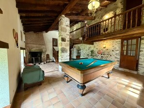 A pool table in a room with stone walls, a wooden ceiling, and a staircase leading to an upper level.