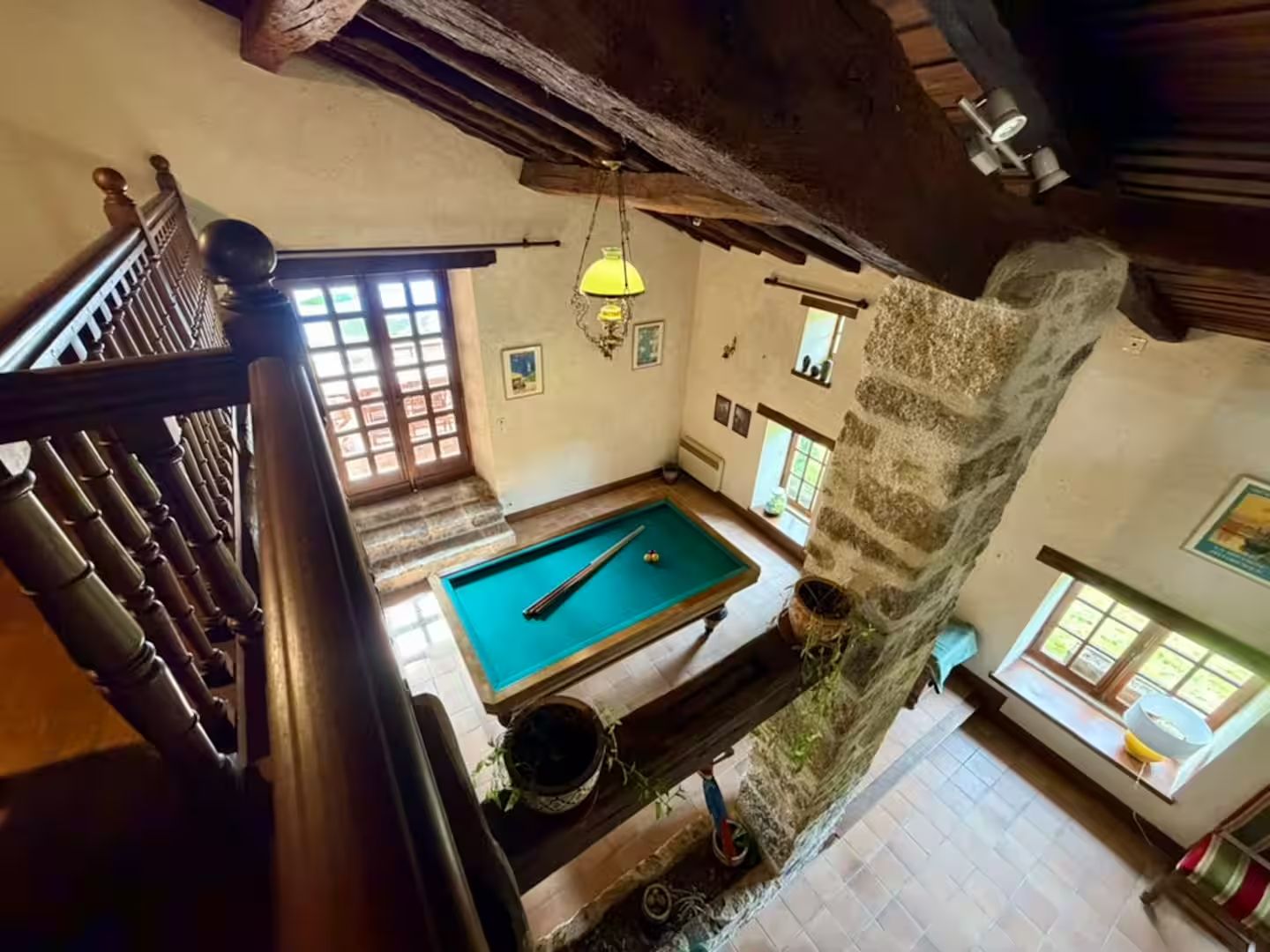 Une pièce avec une table de billard, un escalier et un mur en pierre.