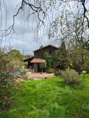A rustic house with a tiled roof, surrounded by lush greenery and a swimming pool.