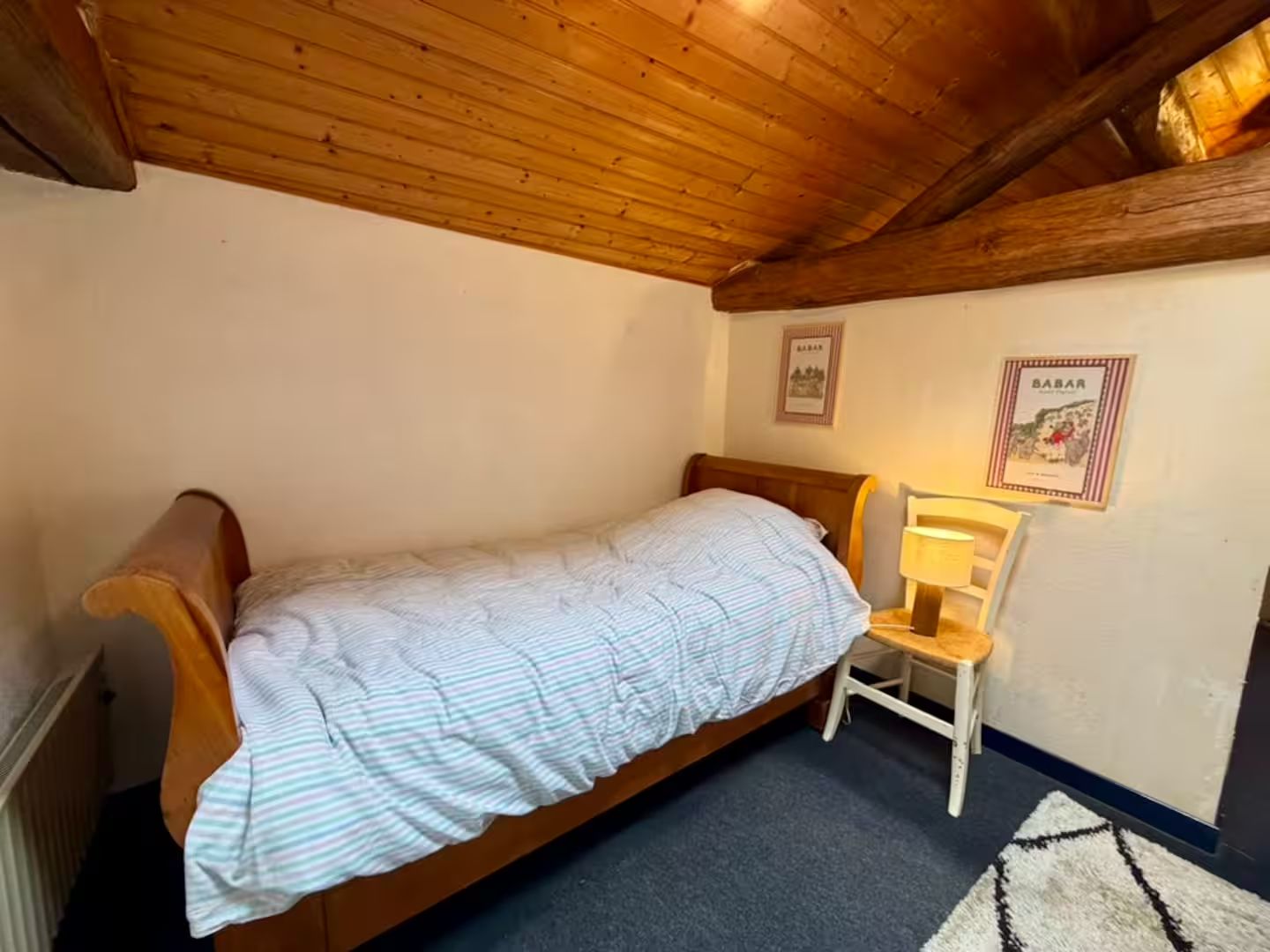 A single bed with a wooden headboard, a small bedside table with a lamp, and two framed pictures on the wall.