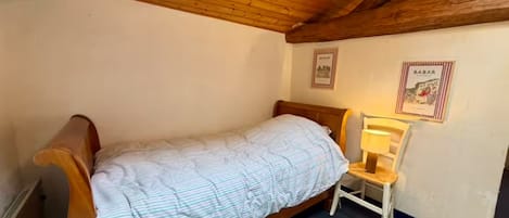 A single bed with a wooden headboard, a small bedside table with a lamp, and two framed pictures on the wall.