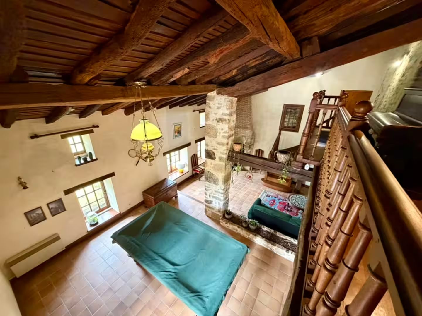 A spacious room with a high ceiling, exposed wooden beams, a large bed, a stone wall, and a view of the outdoors.