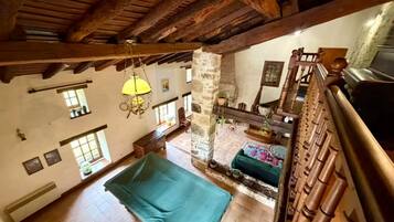 A spacious room with a high ceiling, exposed wooden beams, a large bed, a stone wall, and a view of the outdoors.