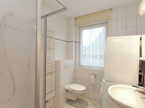 Ein kleines, kompaktes Badezimmer mit Toilette, einer Duschkabine mit Glastür und einem Waschbecken.
