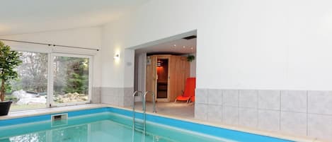 A swimming pool with a clear view of the outdoors, a wooden sauna area, and a red chair.
