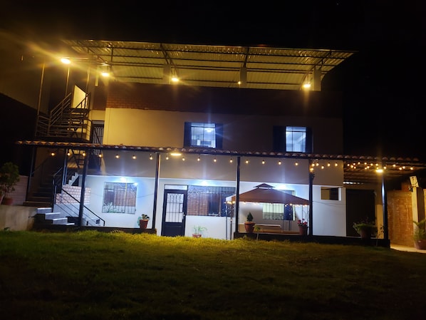 Un edificio de dos pisos con un patio cubierto, asientos al aire libre y luces colgantes.