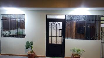 A gated entrance with a black door, two potted plants, and a tiled floor.