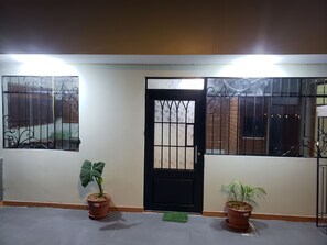 A gated entrance with a black door, two potted plants, and a tiled floor.
