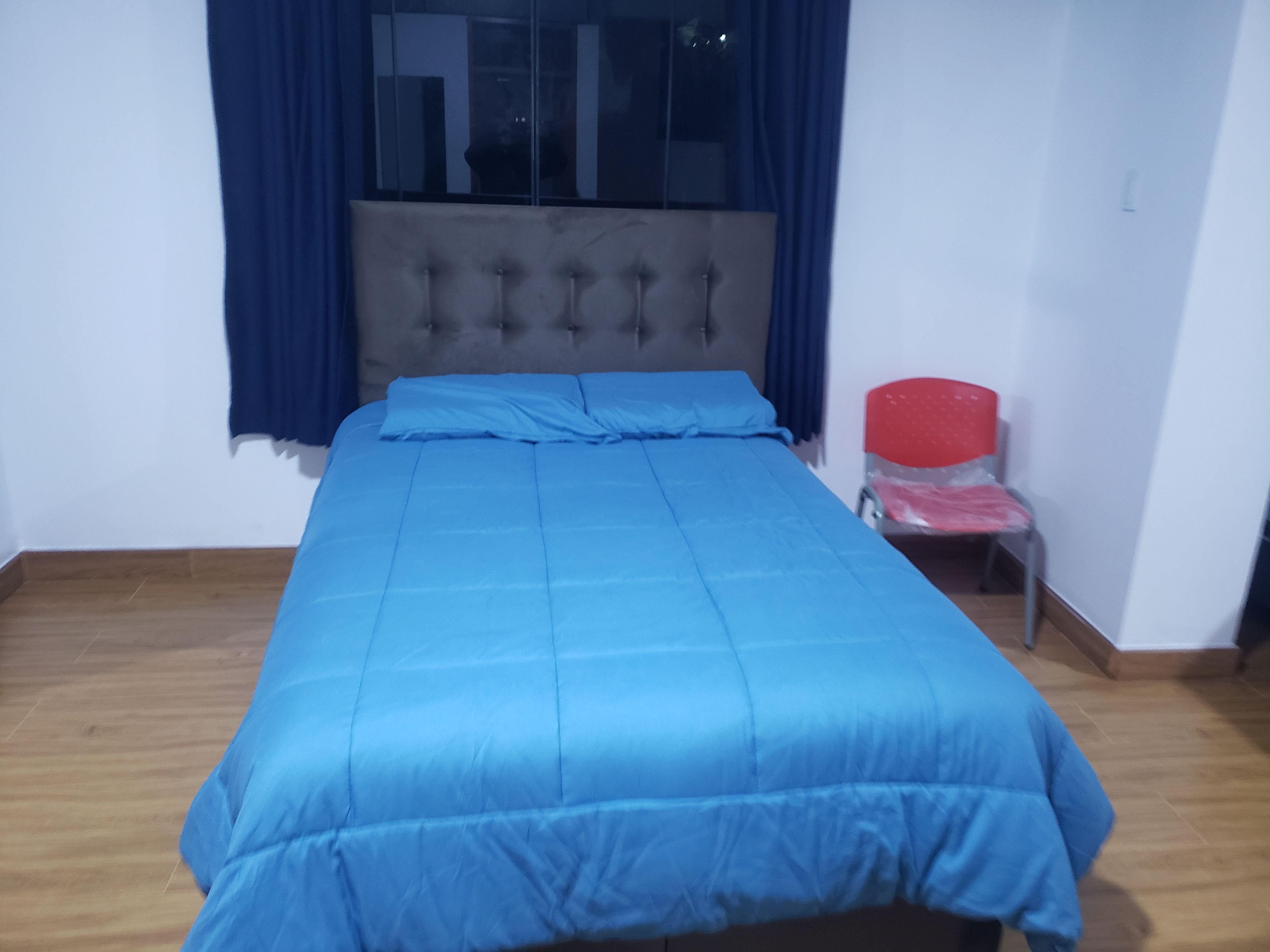 Una habitación con una cama, una ventana con cortinas, una silla y suelo de madera.