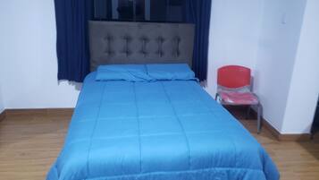 Una habitación con una cama, una ventana con cortinas, una silla y suelo de madera.