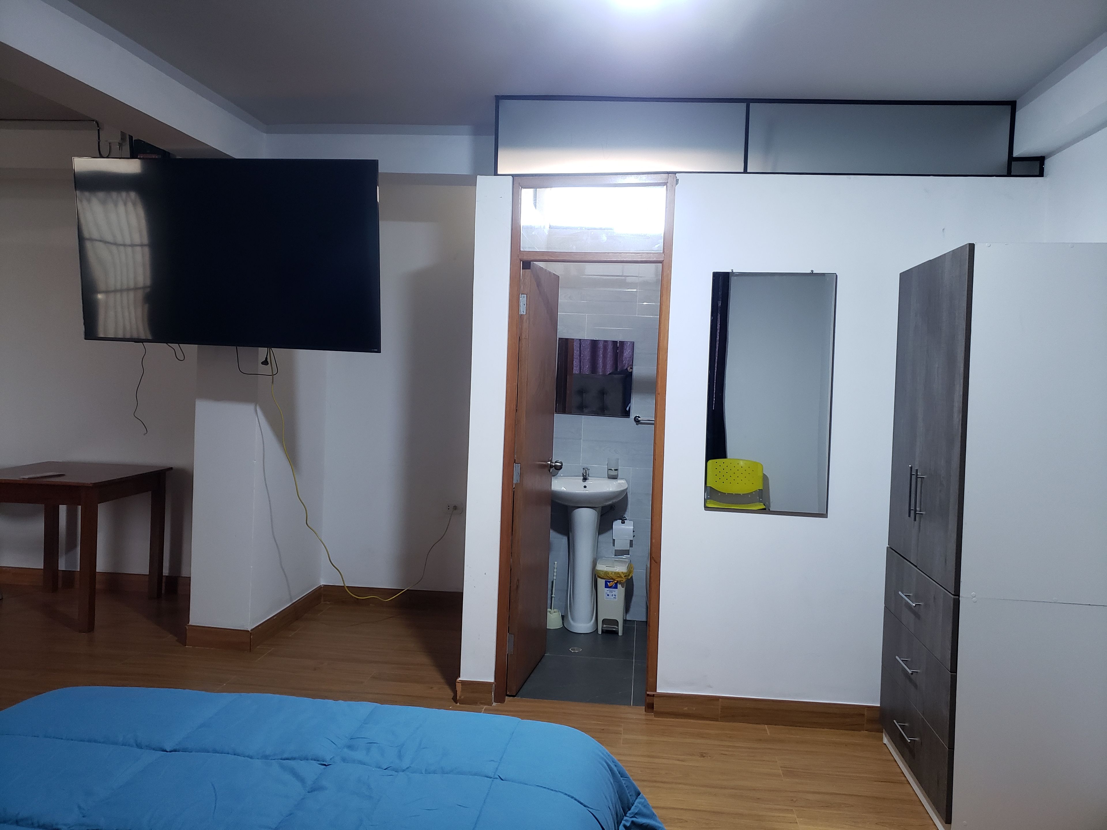 Un dormitorio con cama, televisor, armario y baño visible a través de una puerta abierta.