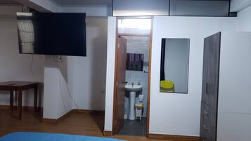 Un dormitorio con cama, televisor, armario y baño visible a través de una puerta abierta.