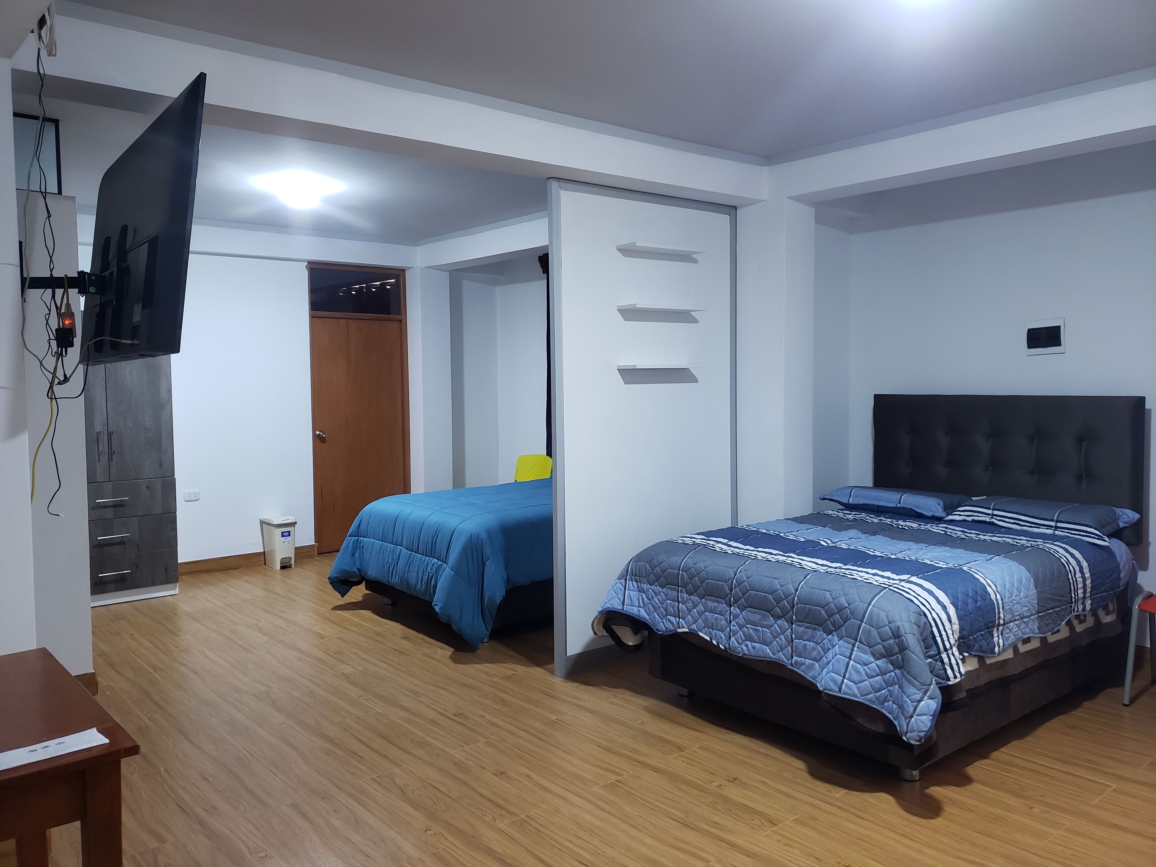 A bedroom with a bed, a desk, a wardrobe, and a television.