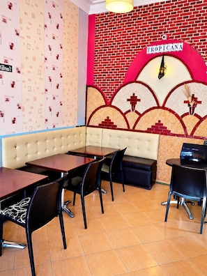 A restaurant interior with a red brick wall, a sign reading 'TROPICANA,' and a seating area with tables and chairs.