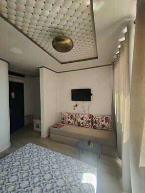 A bedroom with a patterned bedspread, a sofa with floral cushions, a television mounted on the wall, and a ceiling with a decorative element.