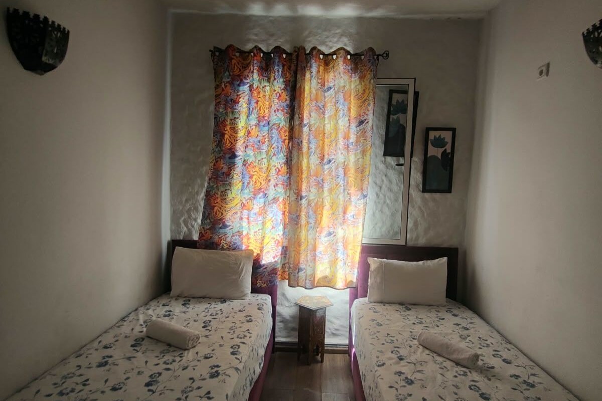 A room with two beds, a small table, and a window with curtains.