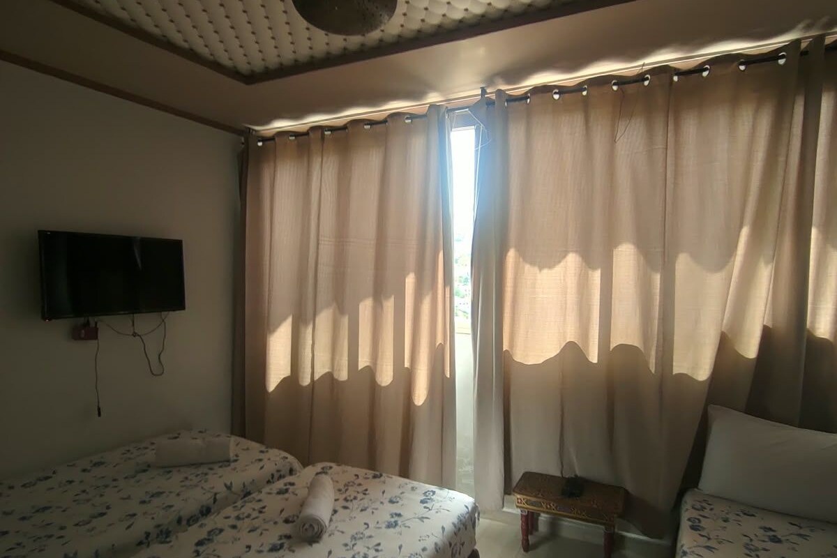 A room with two beds, a flat-screen TV, a small table, and a window with curtains.